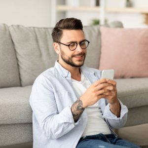 appunti sul cellulare Android, ragazzo al cellulare seduto sotto al divano