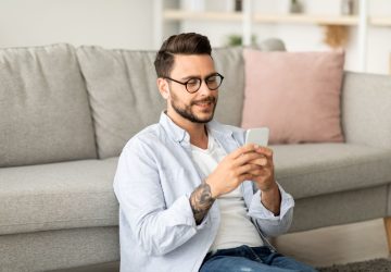 appunti sul cellulare Android, ragazzo al cellulare seduto sotto al divano