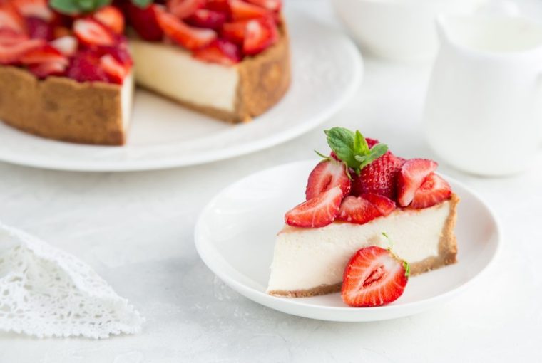Cheesecake alle fragole, una fetta in piatto e il resto sul vassoio