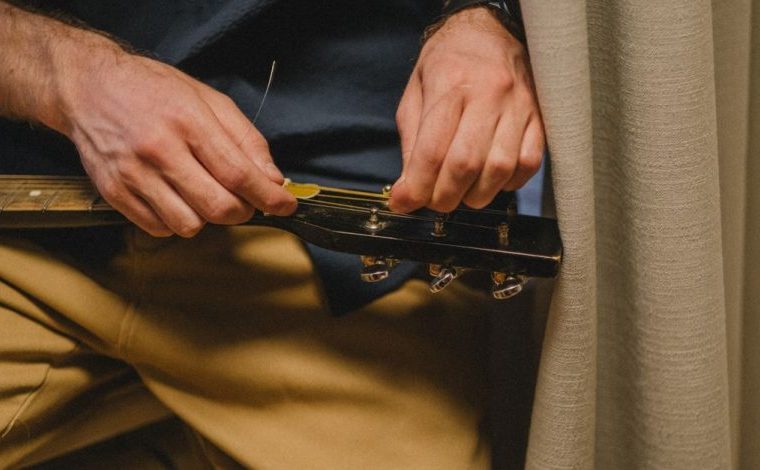 Accordare la chitarra bene richiede metodo e un secondo controllo: Primo piano di un uomo che riaccorda una chitarra…